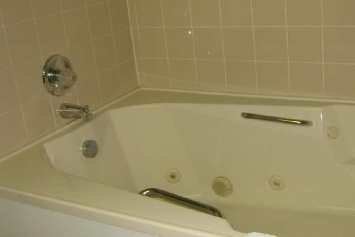 A bathtub with a faucet, a handheld showerhead, and a drain.