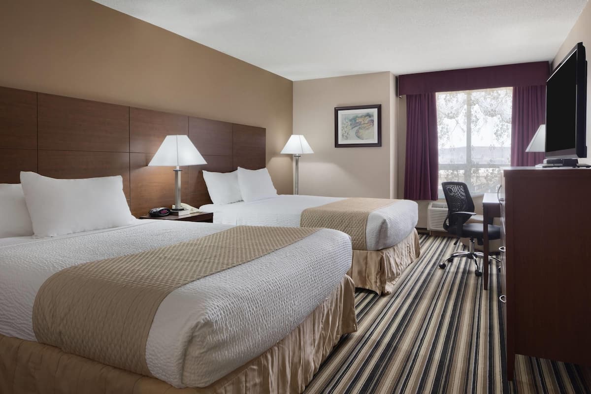 A hotel room with two beds, a desk, a chair, and a television.