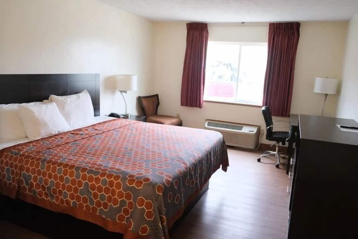 A hotel room with a large bed, a desk, a chair, a lamp, and a window with curtains.
