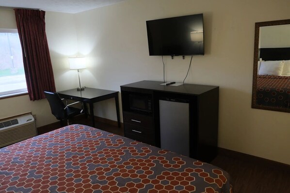 A hotel room with a bed, desk, chair, television, and a heater.