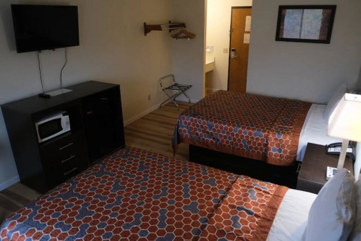 A hotel room with two beds, a TV, a desk with a lamp, and a microwave.