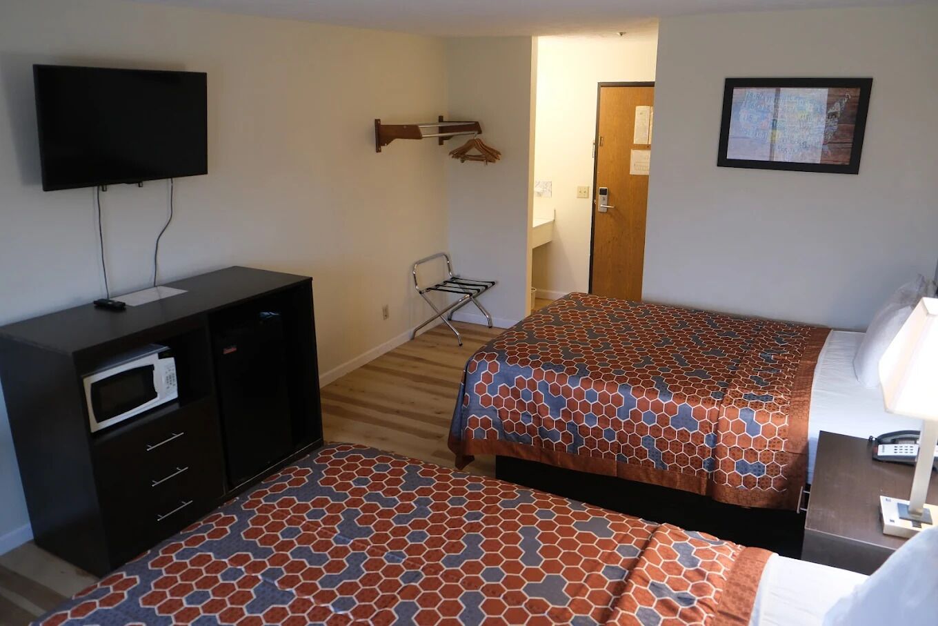 Una camera d'albergo con un letto, una scrivania con una lampada, una TV a parete, un forno a microonde e una sedia.