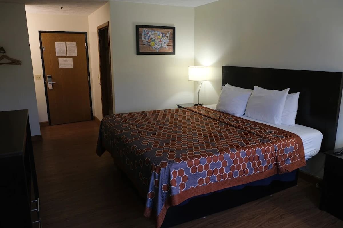 A hotel room with a large bed, a nightstand, a lamp, a door, and a wall map.