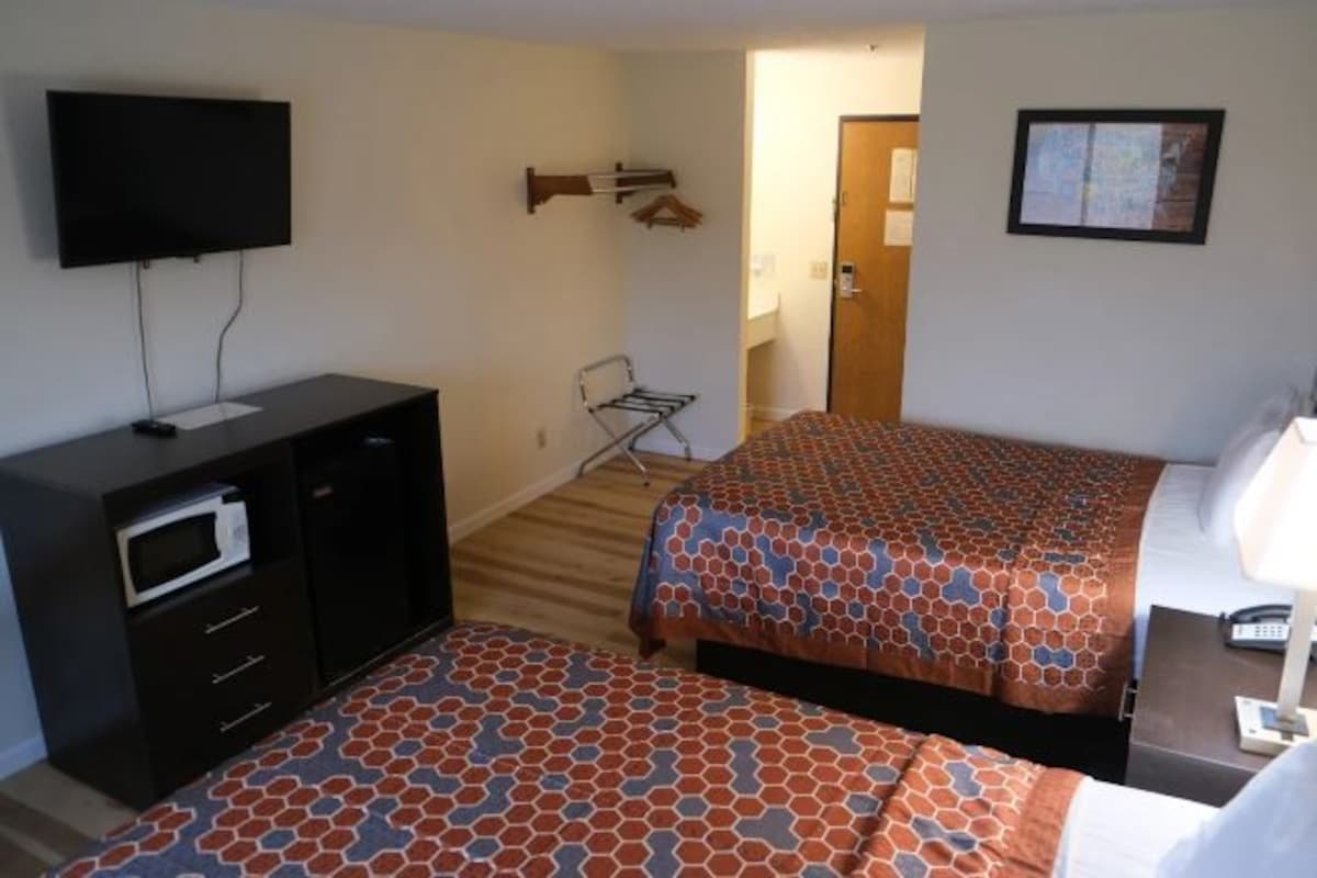 A hotel room with a bed, a desk, a TV, a microwave, and a chair.