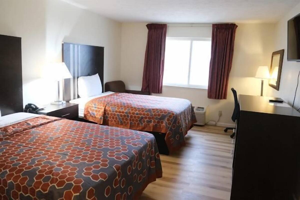 A hotel room with two beds, a desk, a chair, and a window with curtains.