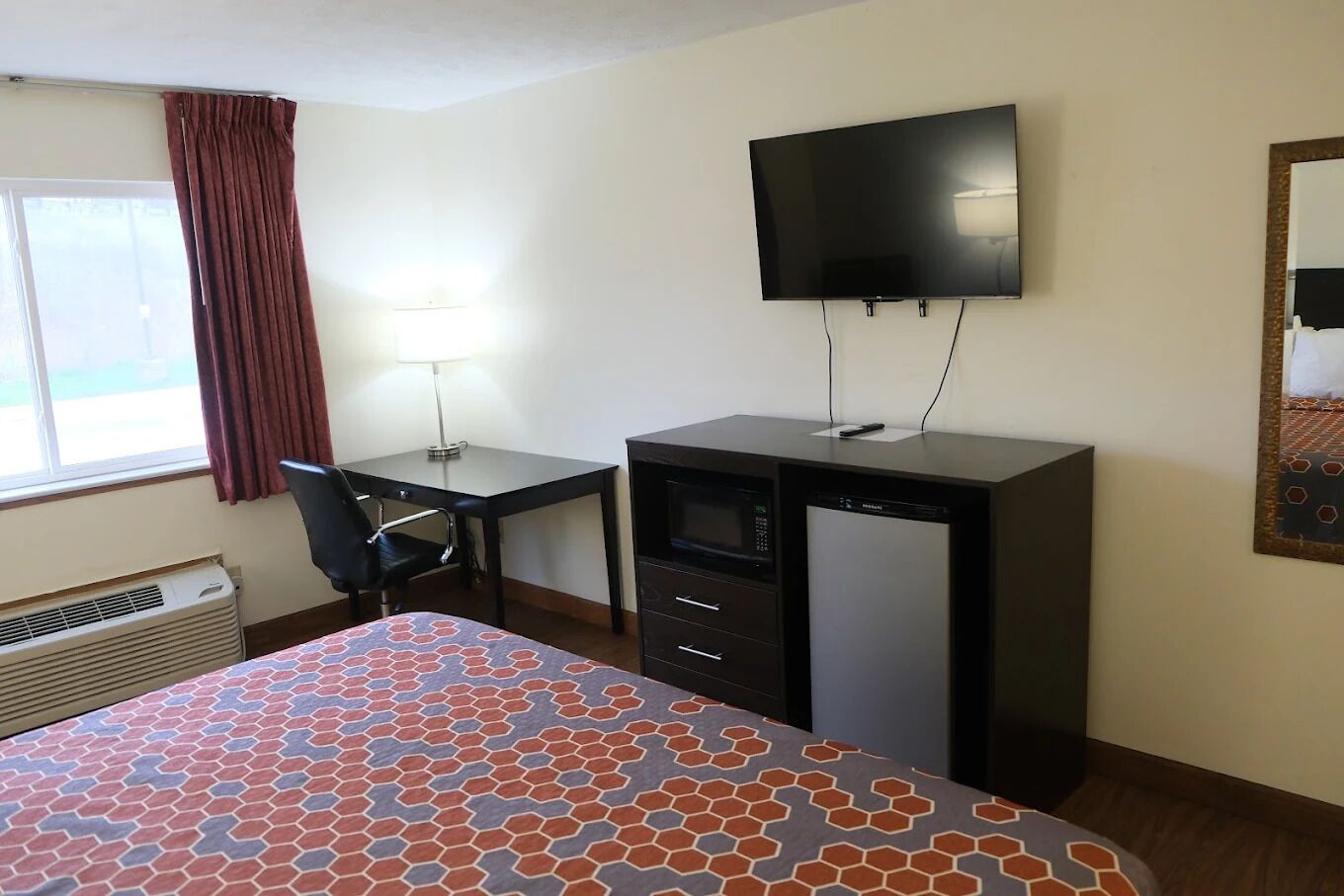 Una habitación de hotel con cama, escritorio, silla, televisor y calefactor.