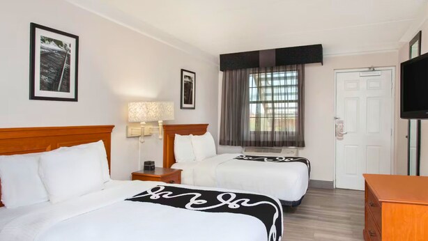 A hotel room with two beds, a TV, a wooden dresser, and a window with curtains. - Baymont by Wyndham Fort Myers Central (Fort Myers)