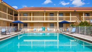 A hotel with a swimming pool, multiple balconies, and lounge chairs. - Baymont by Wyndham Fort Myers Central (Fort Myers)