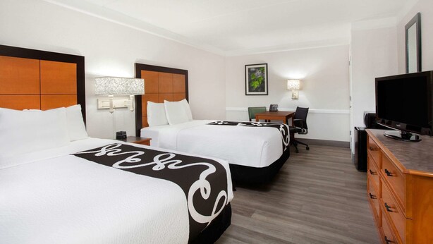 A hotel room with two beds, a desk, a television, and a dresser. - Baymont by Wyndham Fort Myers Central (Fort Myers)
