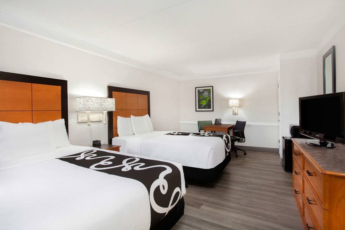 A hotel room with two beds, a desk, a television, and a dresser.