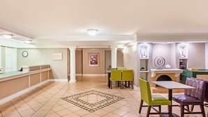 A hotel lobby with a reception desk, a dining area with tables and chairs, and a decorative rug. - Baymont by Wyndham Fort Myers Central (Fort Myers)