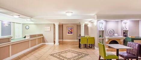 Un hall de hotel con mostrador de recepción, un comedor con mesas y sillas, y una alfombra decorativa.