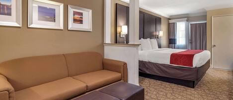 A hotel room with a brown sofa, a bed with a red blanket, and three framed pictures on the wall.