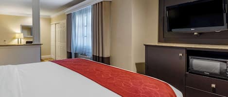 Une chambre d’hôtel avec un grand lit, un téléviseur à écran plat, un four à micro-ondes et une commode.