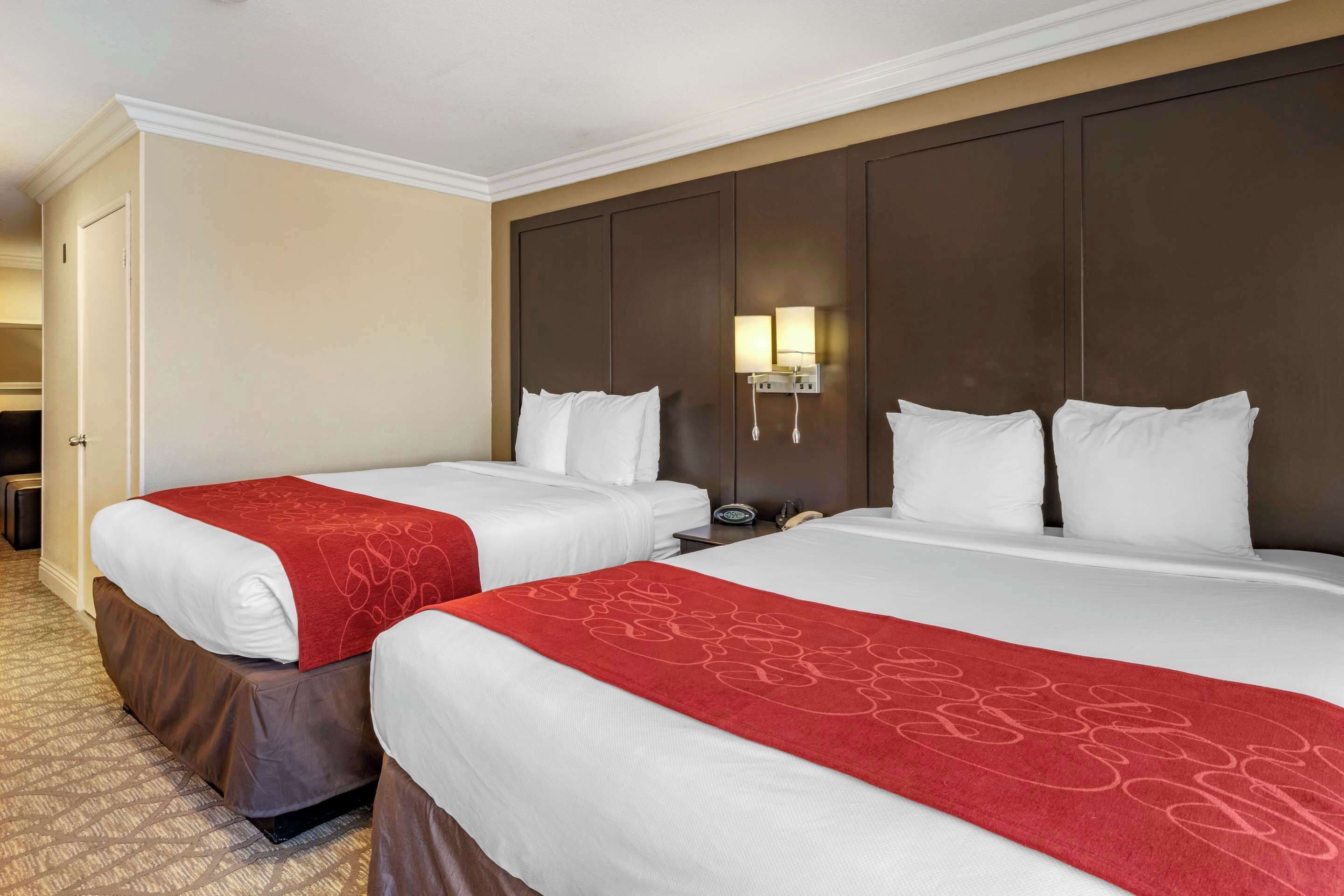 A hotel room with two beds, a large dark wood headboard, a red decorative runner, and a wall-mounted phone.