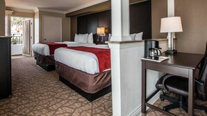 A hotel room with two beds, a desk, a chair, a coffee maker, and a lamp.