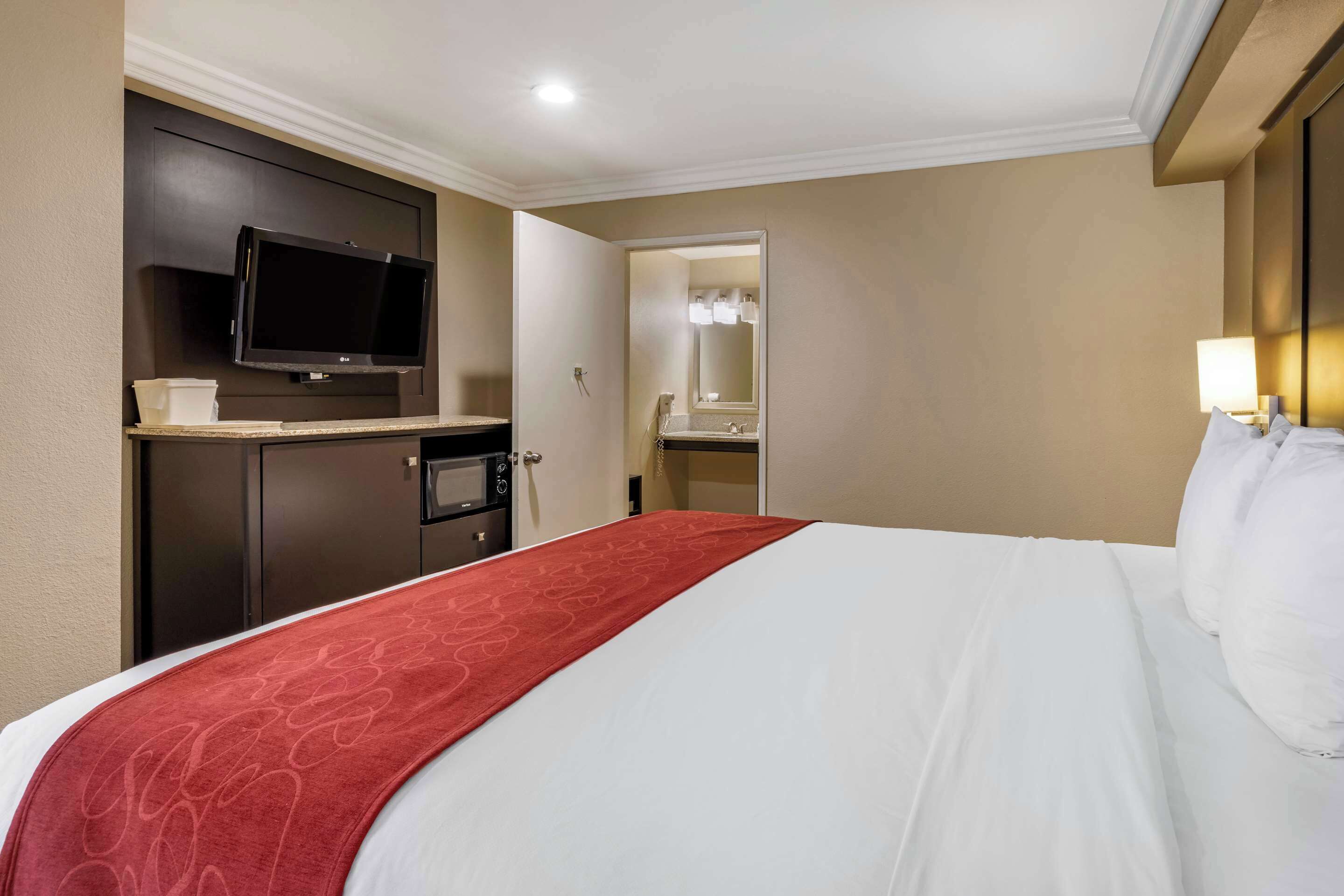 A hotel room with a bed, a TV, a desk, and a bathroom visible through an open door.
