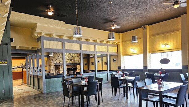 A restaurant with wooden flooring, multiple tables and chairs, a stone fireplace, and hanging pendant lights. - Travelodge by Wyndham Prince Albert (Prince Albert)