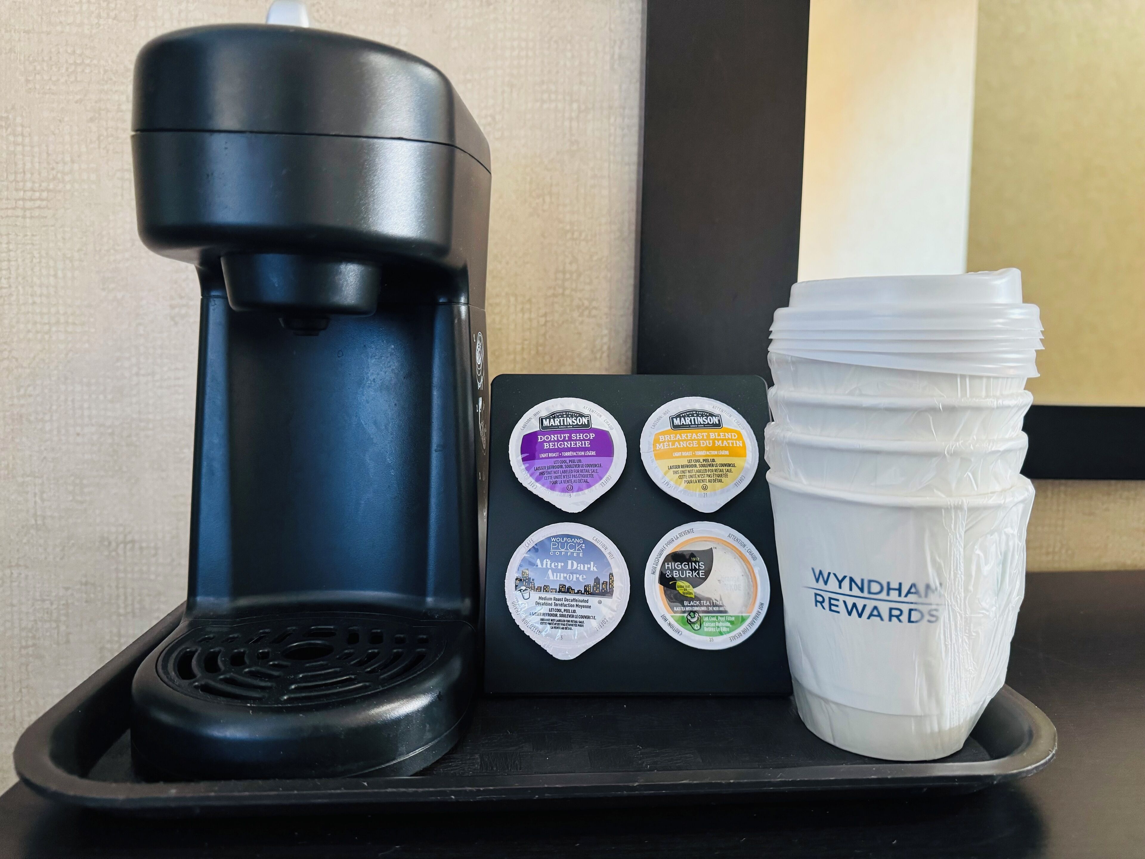 A coffee maker, a tray with coffee pods, and a stack of coffee cups on a table.
