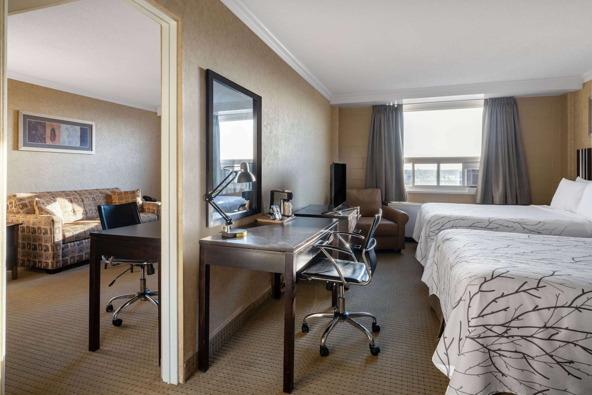 Une chambre d’hôtel comprenant un lit, un bureau avec une chaise, un canapé et une grande fenêtre avec des rideaux.