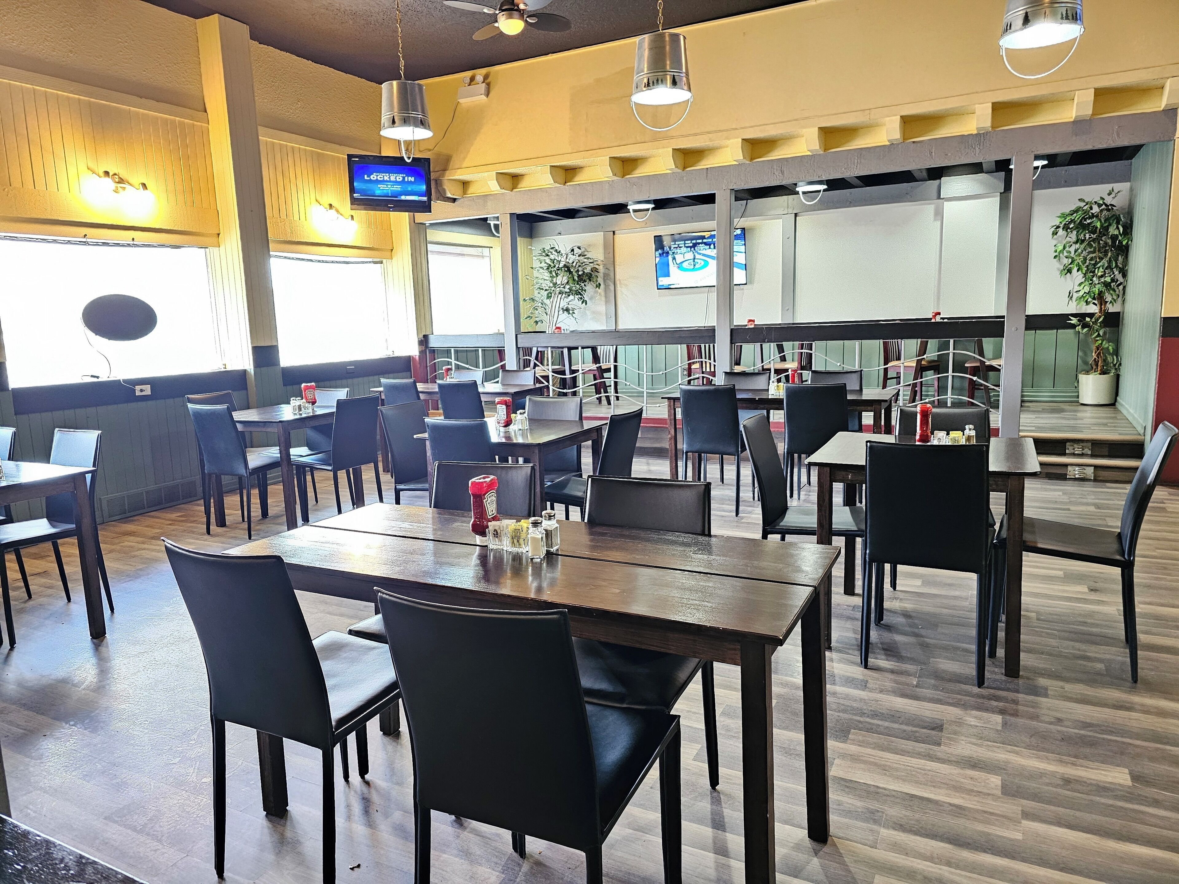 Un restaurante espacioso con varias mesas y sillas, ventiladores de techo y amplios ventanales.