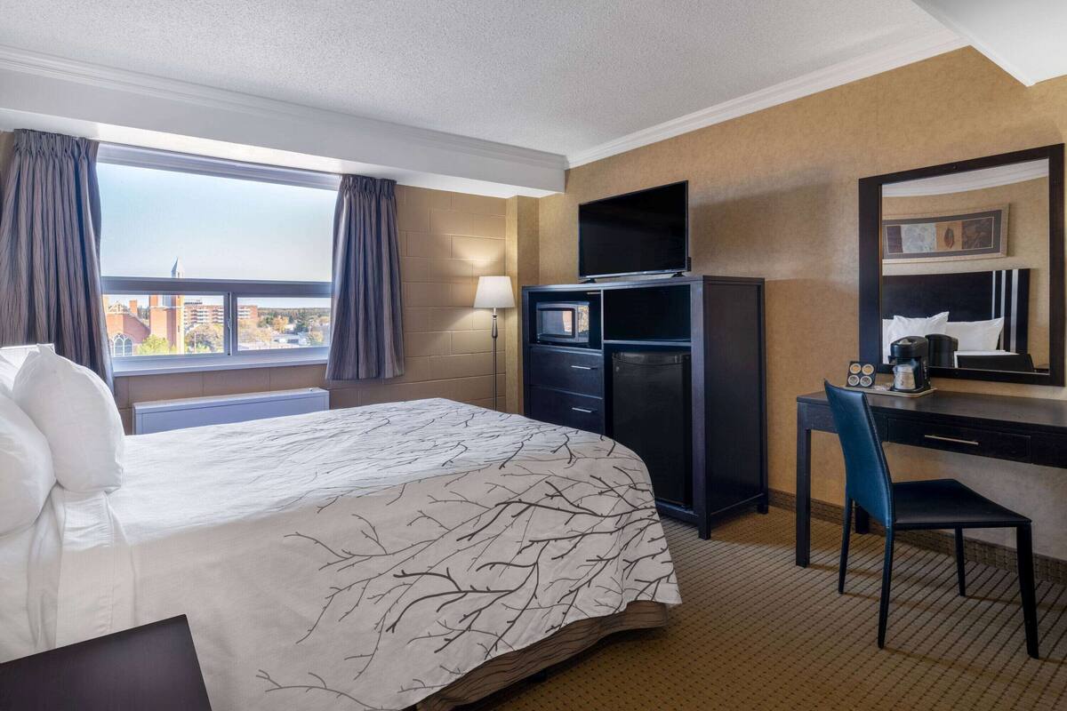 Une chambre d’hôtel avec un grand lit, un bureau avec une chaise, une télévision et une fenêtre avec des rideaux.