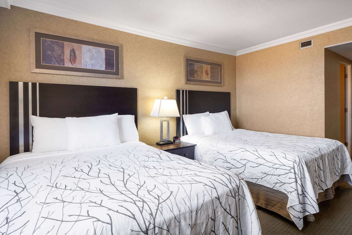 Une chambre d’hôtel avec deux lits, chacun doté d’une tête de lit, d’une table de chevet avec une lampe et d’œuvres d’art encadrées accrochées au mur.