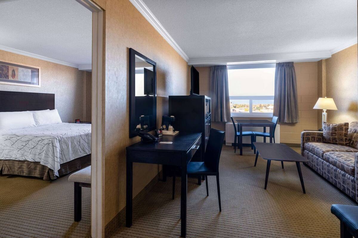 Une chambre d’hôtel comprenant un lit, un bureau avec une chaise, un canapé, une télévision et une fenêtre avec des rideaux.