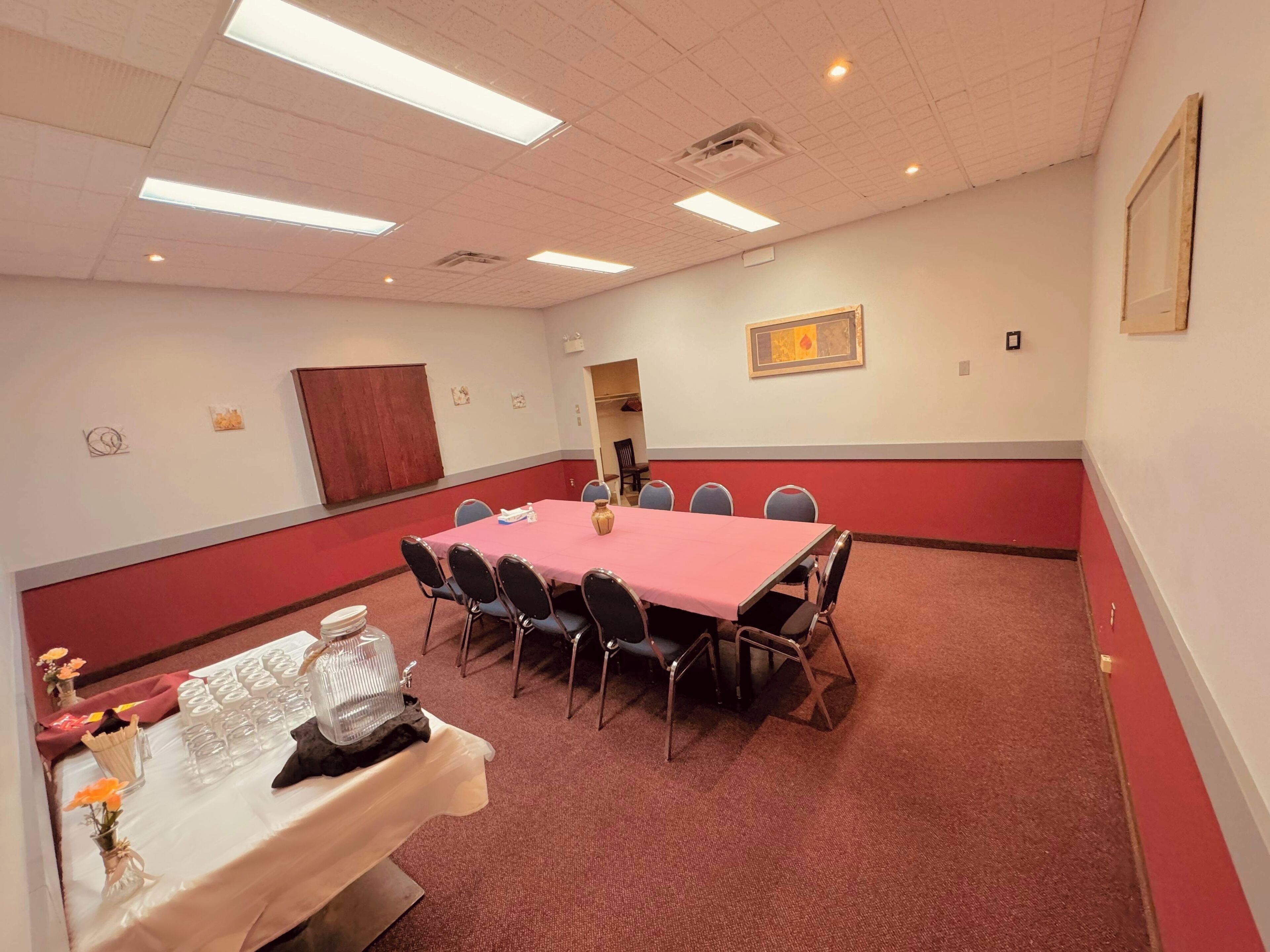 A conference room with a red carpet, a long table with chairs, and a white table with flowers.