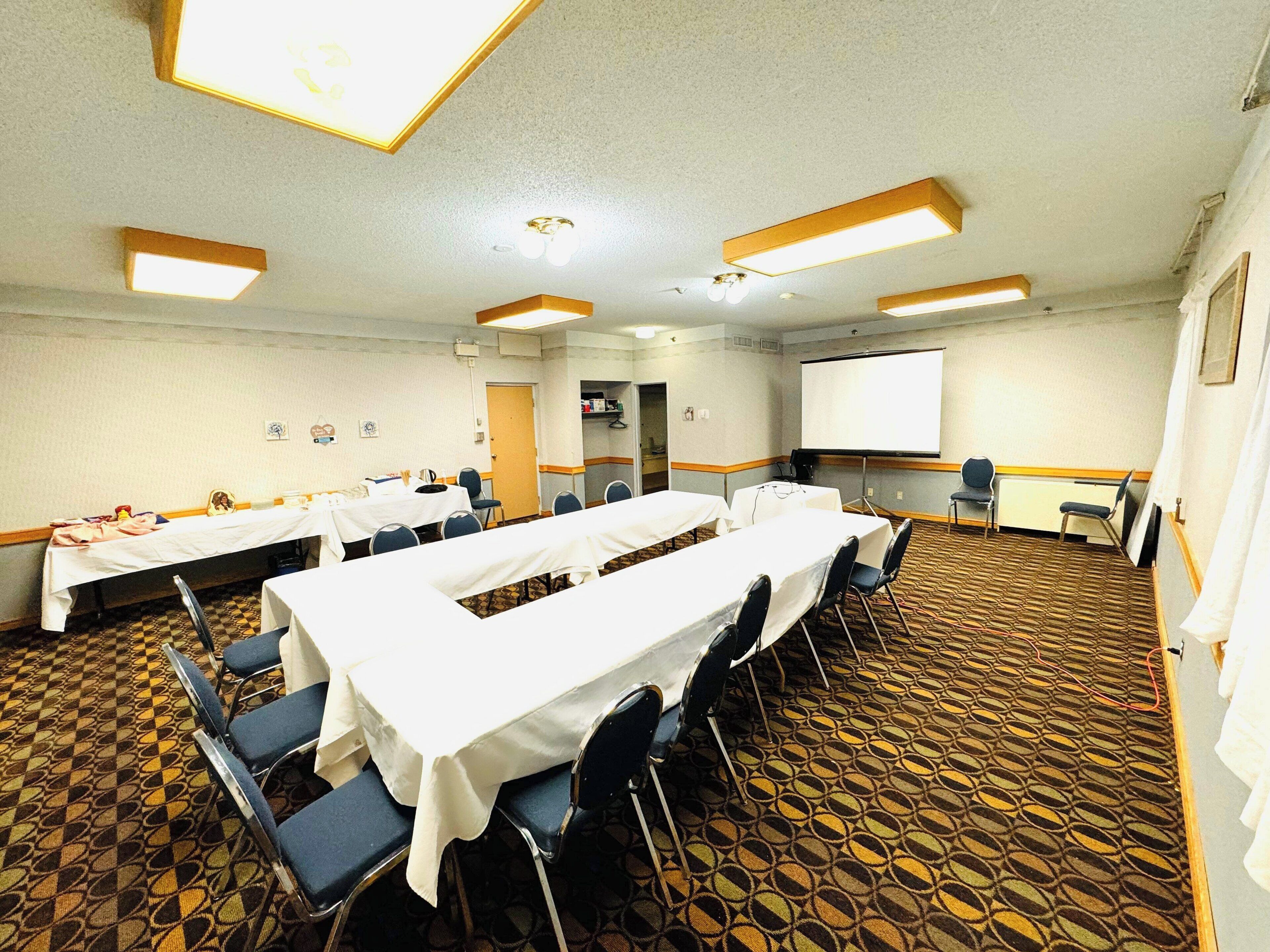 A conference room with multiple tables, chairs, a projector screen, and a carpeted floor.
