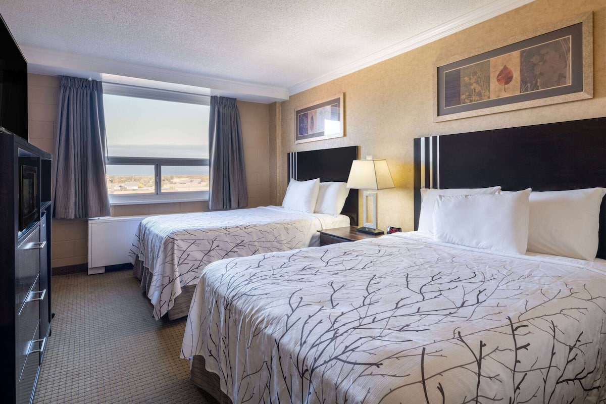 Une chambre d’hôtel avec deux lits, une télévision, un bureau et une fenêtre avec des rideaux.