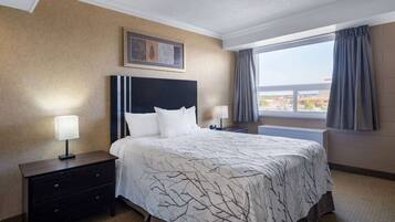 A hotel room with a large bed, a nightstand with a lamp, a framed picture on the wall, and a window with curtains.