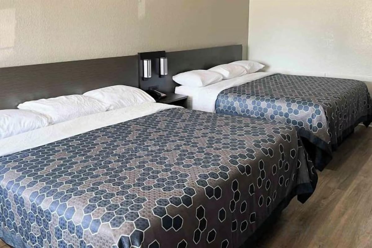 Habitación de hotel con dos camas, cada una con una colcha estampada, una mesita de noche con lámpara, e iluminación empotrada en la pared.