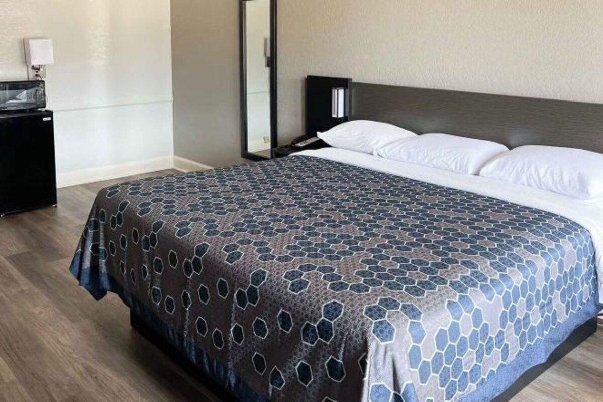 A hotel room with a bed, a nightstand, a lamp, and a mirror.