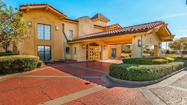 A large, yellow building with a red-tiled roof, a covered entrance, and a brick-paved driveway.