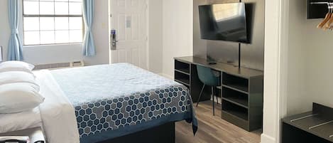 A hotel room with a bed, a desk, a chair, a TV, and a wardrobe.