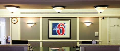 A reception desk with a framed sign for a motel, a clock, and a door marked "Employee Only".