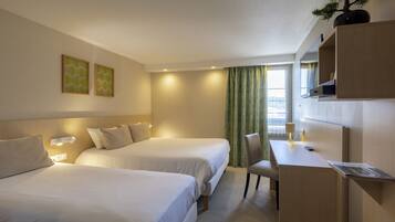 A hotel room with two beds, a desk, a chair, and a potted plant.