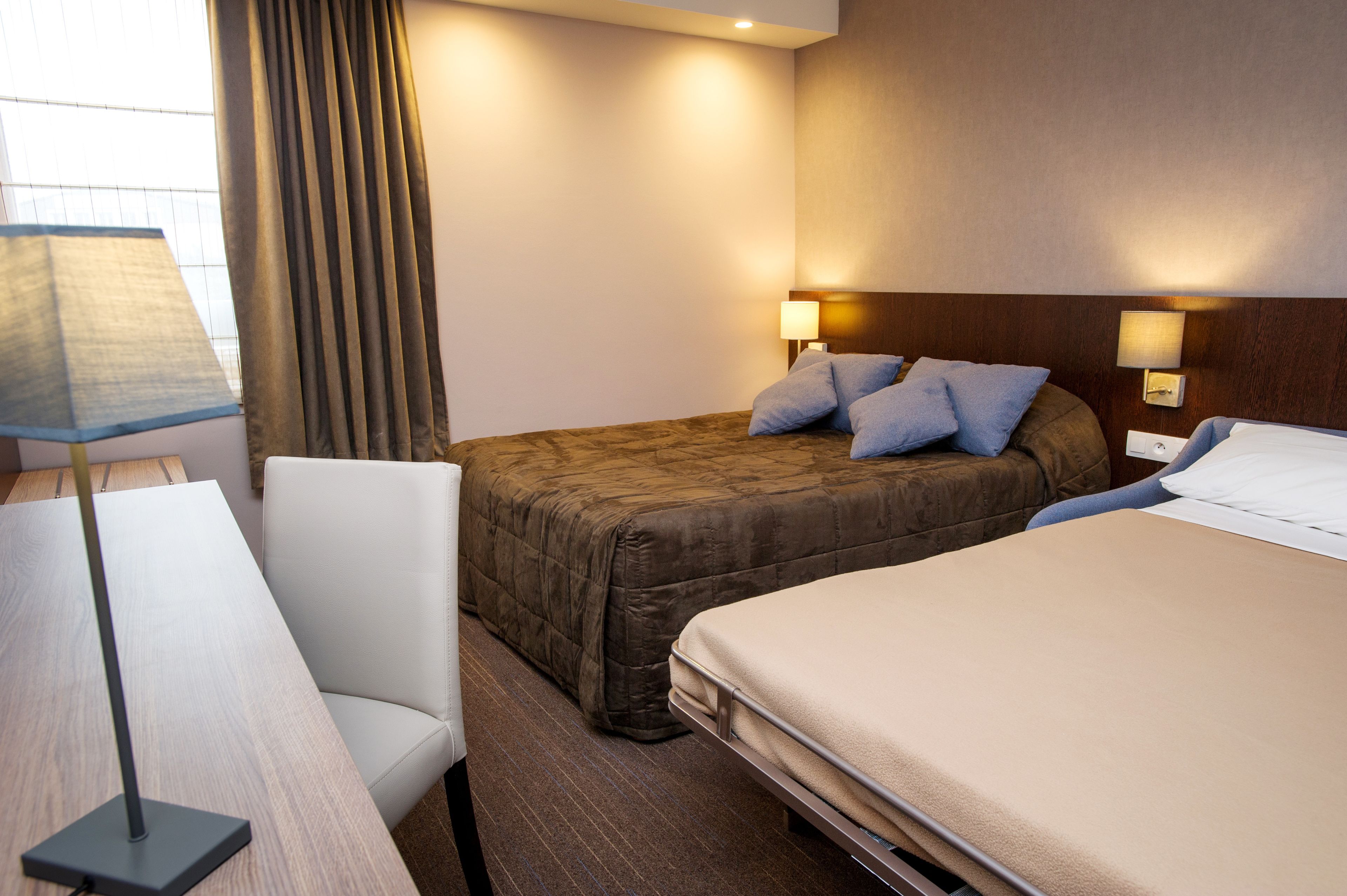 A hotel room with a large bed, a smaller bed, a desk, and a chair.