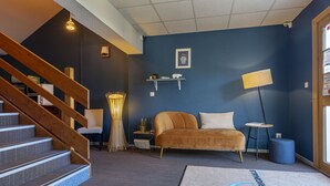 A modern living room with a blue accent wall, a sofa, a lamp, and a staircase. - The Originals City Hotel Limoges Sud (Feytiat)