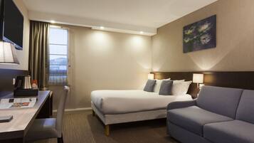 A hotel room with a bed, a sofa, a desk, and a TV.