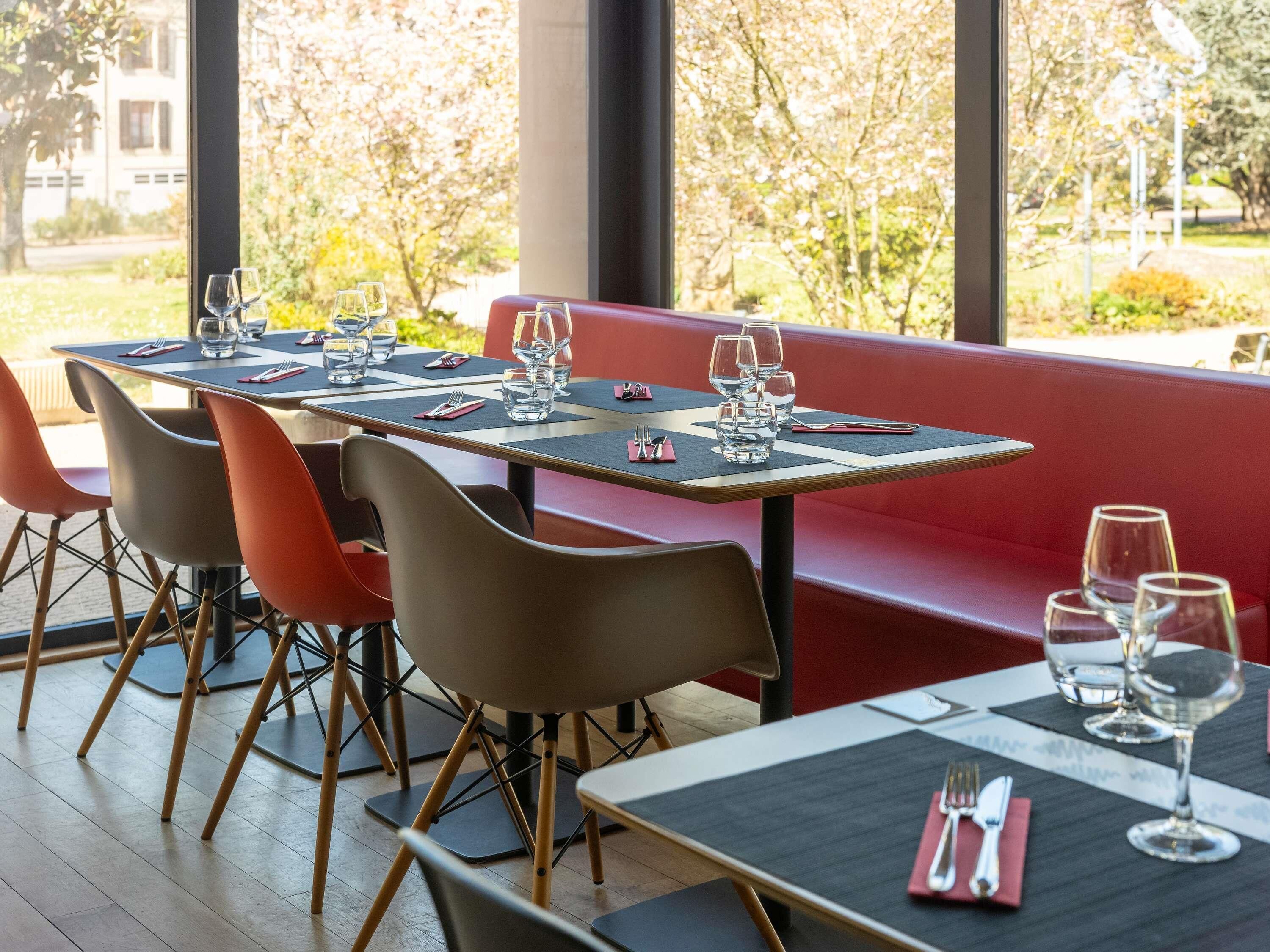 A restaurant with tables set for dining, chairs, and a red bench.
