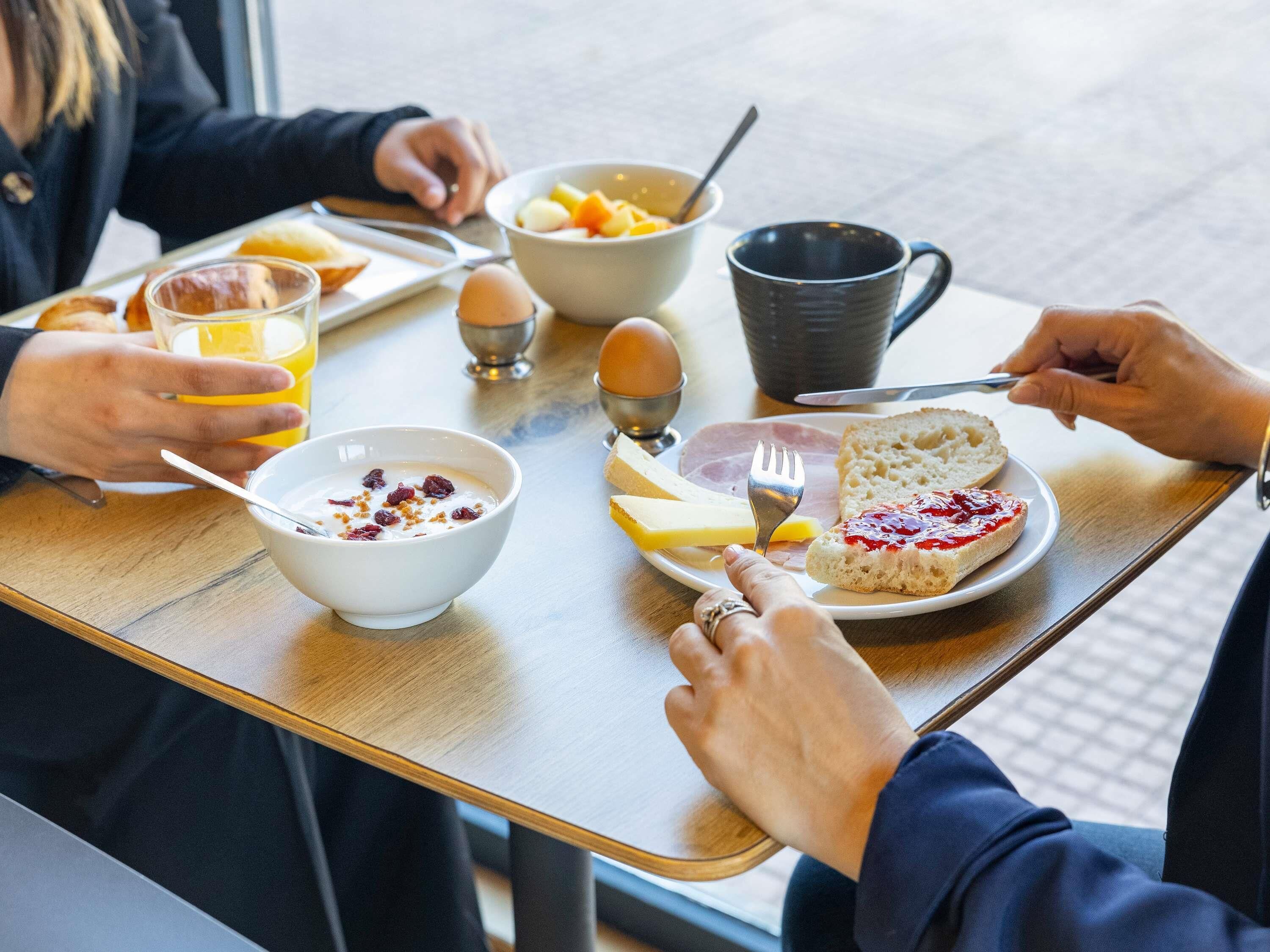 A breakfast table with a plate of toast, jam, cheese, and a bowl of cereal with fruit.