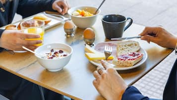 A breakfast table with a plate of toast, jam, cheese, and a bowl of cereal with fruit.