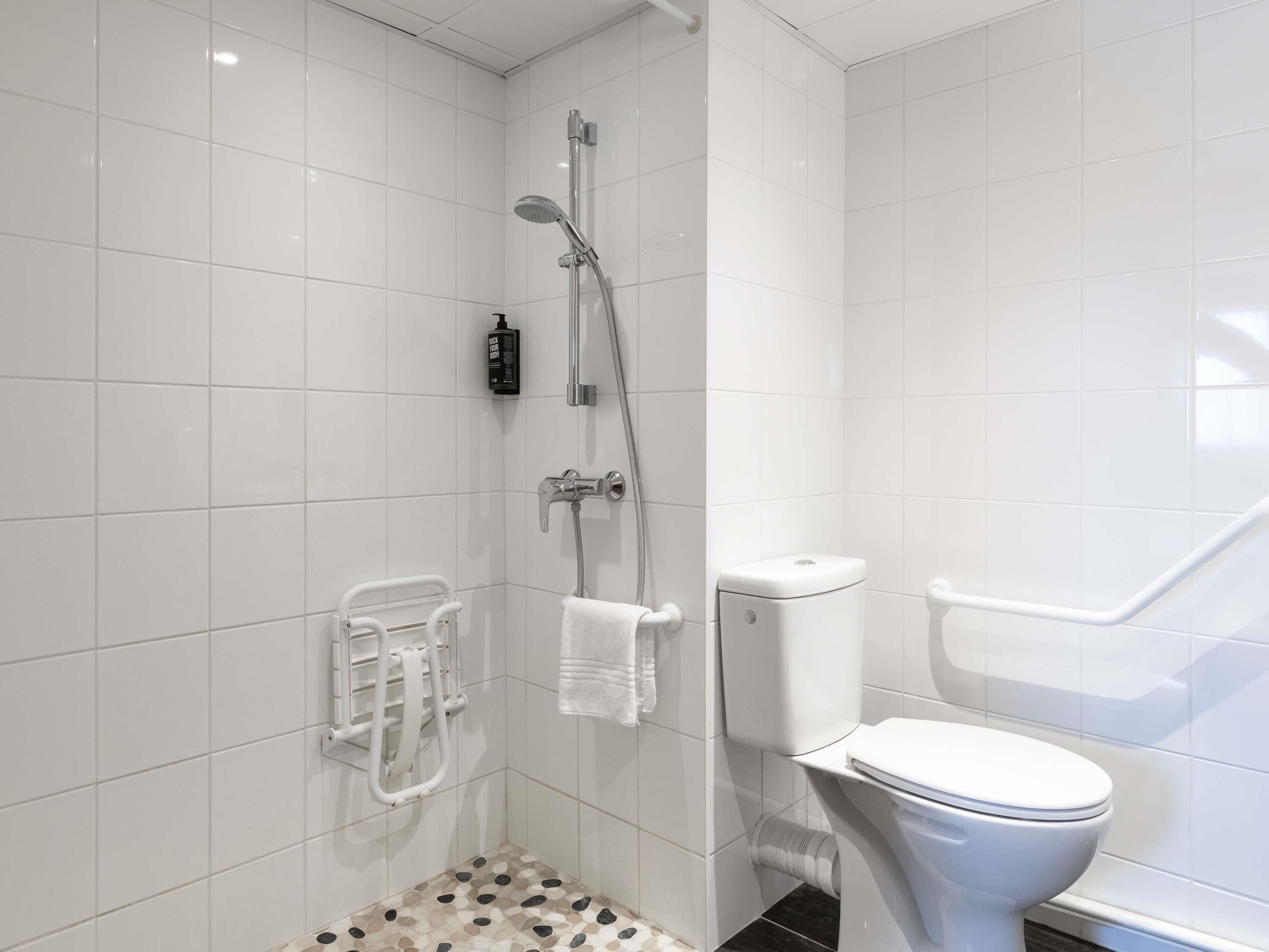 A modern bathroom with white tiles, a shower, a toilet, and a hand dryer.
