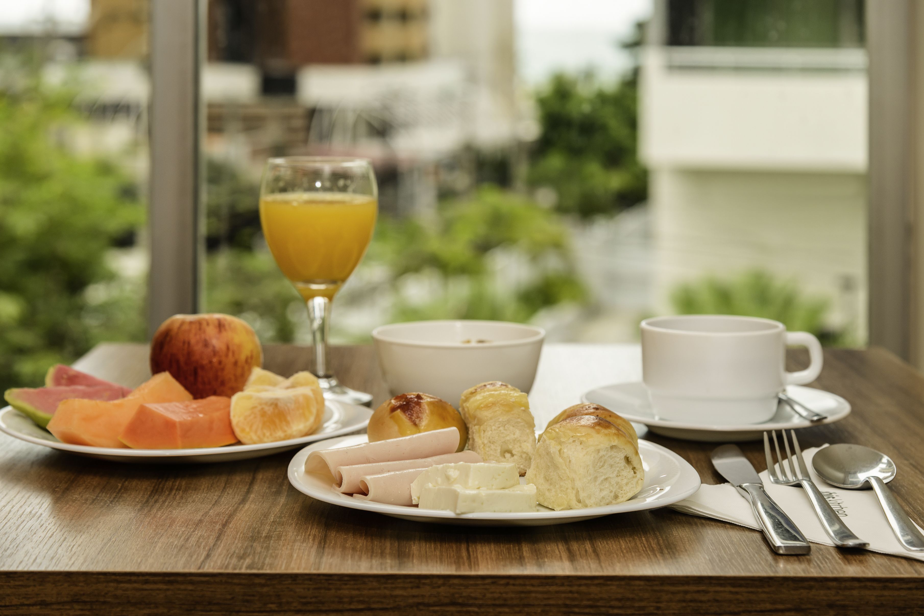 A breakfast table with a plate of fruit, croissants, and a glass of orange juice.