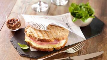 Un sándwich sobre una tabla de pizarra, con un tenedor y un cuchillo a un lado.