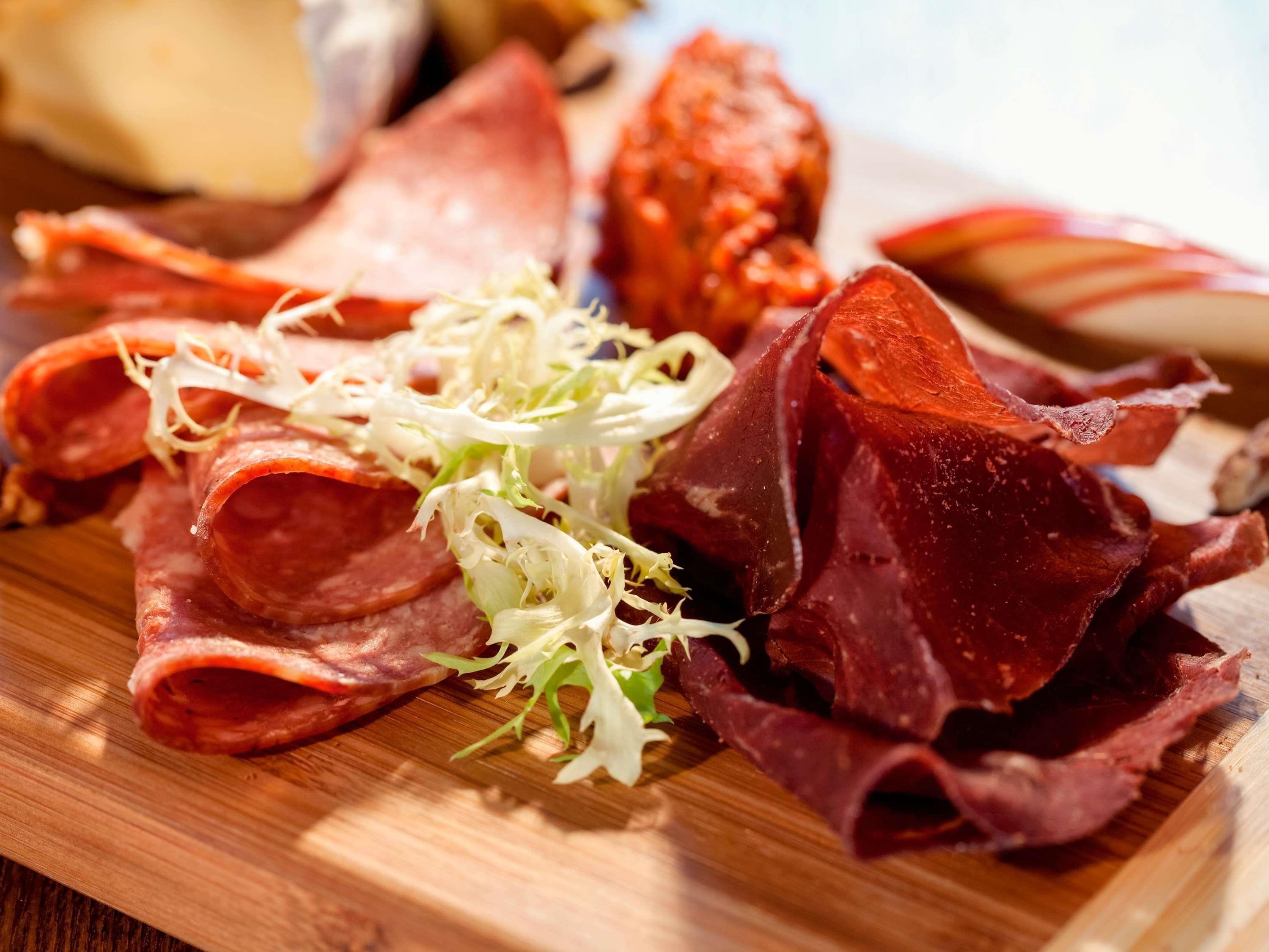 A wooden board with various cured meats and shredded lettuce.