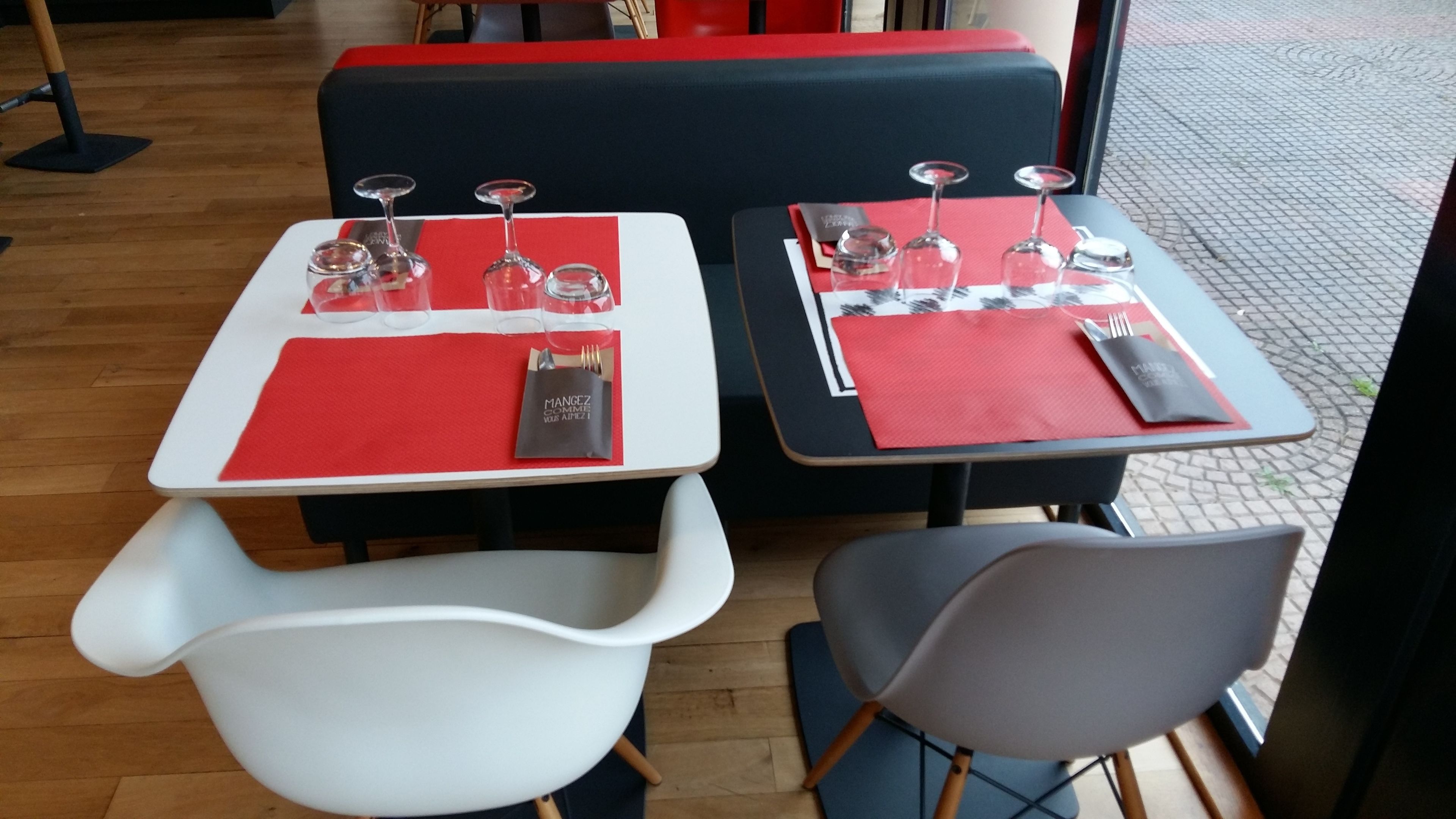 Two tables with red placemats and wine glasses, a white chair, and a grey chair.