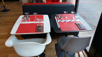 Two tables with red placemats and wine glasses, a white chair, and a grey chair.
